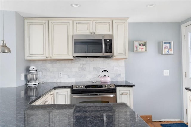 kitchen featuring cream cabinets, appliances with stainless steel finishes, decorative backsplash, and dark stone counters