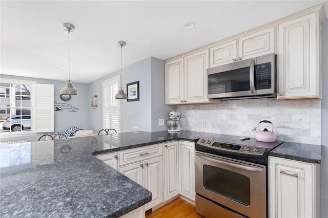 kitchen with stainless steel appliances, hanging light fixtures, cream cabinets, and backsplash