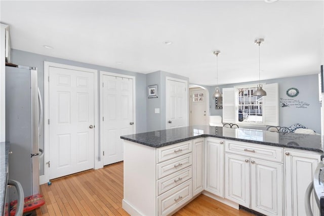 kitchen with light wood-style flooring, white cabinets, decorative light fixtures, and freestanding refrigerator