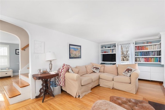 living room featuring arched walkways, light wood finished floors, and stairs