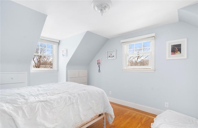 bedroom with vaulted ceiling, light wood finished floors, multiple windows, and baseboards