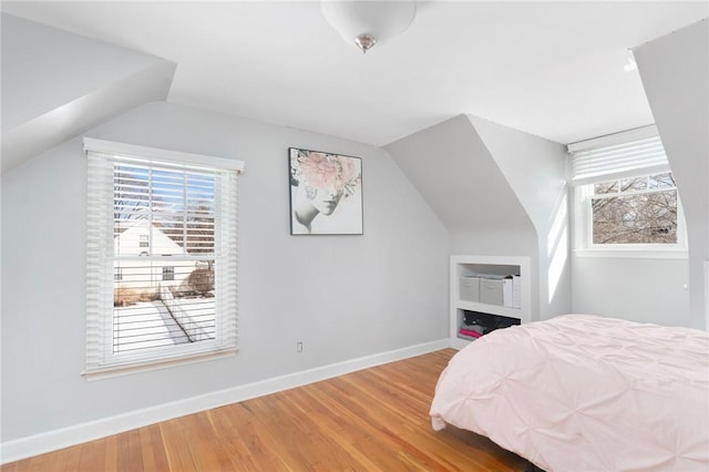 bedroom with vaulted ceiling, multiple windows, wood finished floors, and baseboards