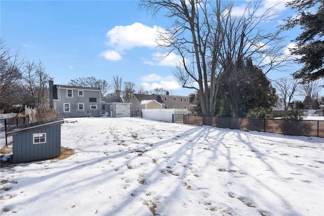 yard layered in snow featuring a shed, a residential view, fence, and an outbuilding