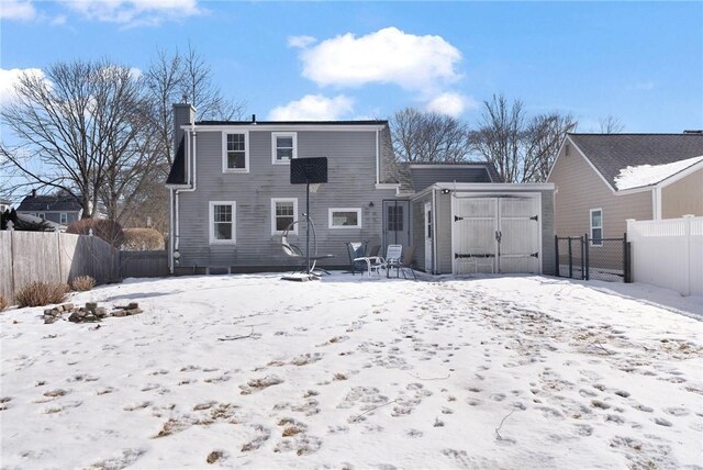 snow covered property with an outbuilding, a chimney, a storage shed, a garage, and a fenced backyard