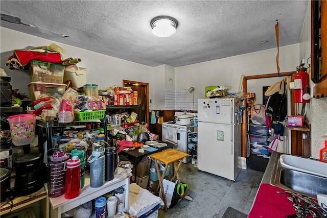 kitchen featuring a sink, concrete floors, a textured ceiling, and freestanding refrigerator