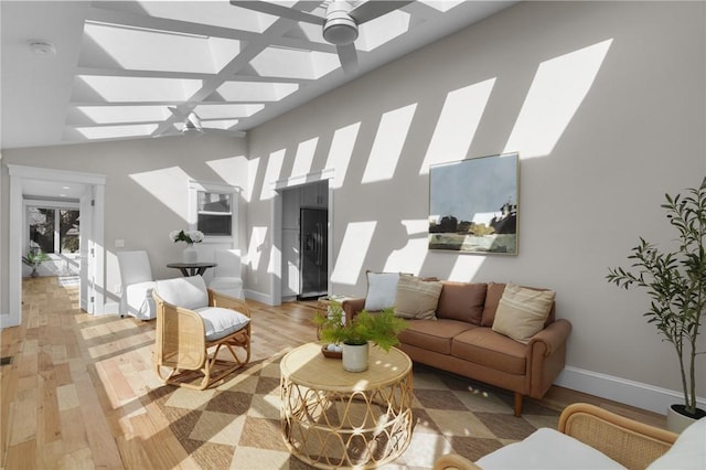 living room featuring a skylight, light wood finished floors, ceiling fan, high vaulted ceiling, and baseboards