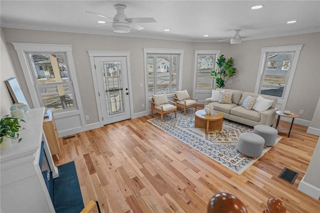 living room with a healthy amount of sunlight, visible vents, crown molding, and light wood finished floors