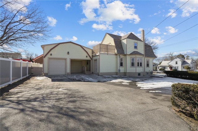 view of front of house with aphalt driveway, a shingled roof, a gambrel roof, fence, and a garage