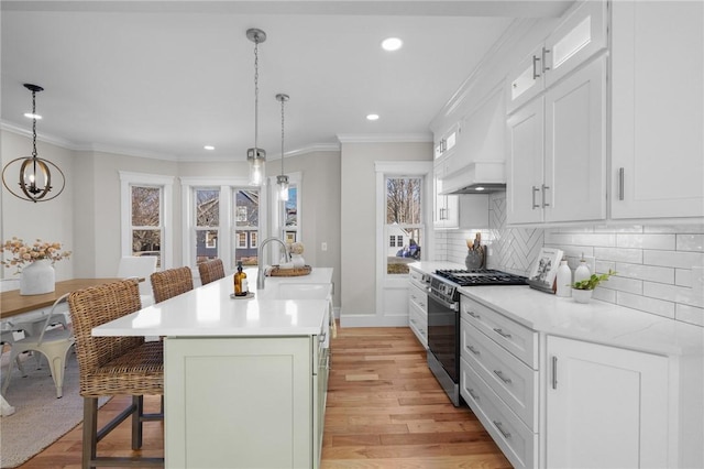 kitchen featuring gas stove, decorative light fixtures, a center island with sink, and a kitchen bar