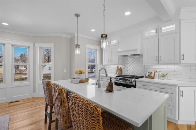 kitchen with premium range hood, an island with sink, stainless steel range with gas cooktop, and white cabinets