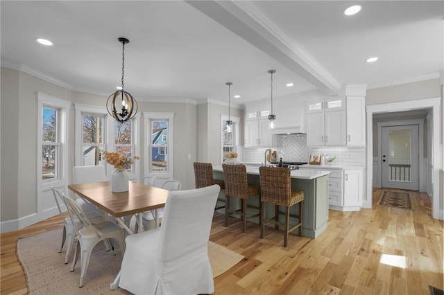 dining space featuring a healthy amount of sunlight, light wood-style flooring, ornamental molding, and beam ceiling