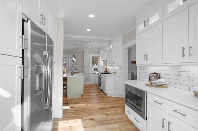 kitchen featuring appliances with stainless steel finishes, white cabinetry, crown molding, and decorative light fixtures