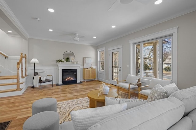 living area with visible vents, stairway, ornamental molding, light wood-style floors, and ceiling fan