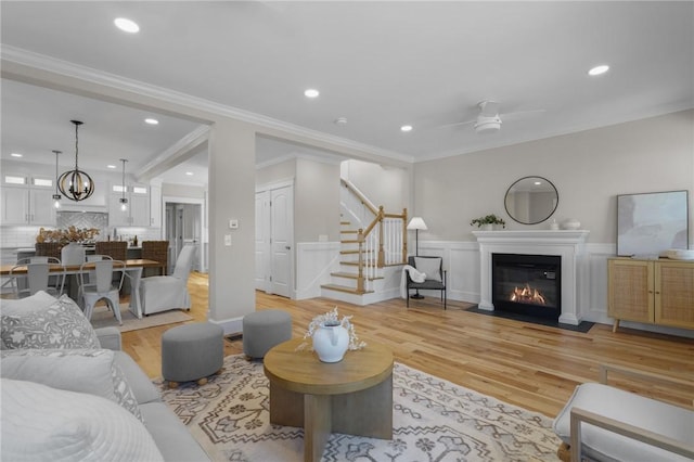 living room with light wood finished floors, a fireplace with flush hearth, stairway, and a wainscoted wall