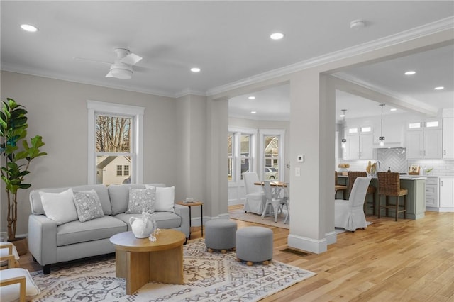 living room featuring light wood-type flooring, plenty of natural light, baseboards, and crown molding