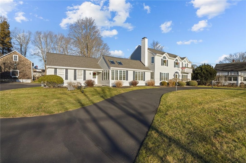 view of front of home featuring a front lawn, a chimney, and aphalt driveway