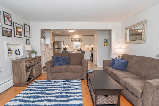 living area with light wood finished floors, baseboard heating, rail lighting, and a decorative wall