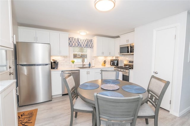 kitchen with light countertops, light wood-style flooring, backsplash, appliances with stainless steel finishes, and white cabinetry