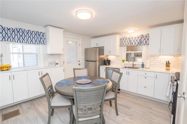 kitchen featuring light wood-style flooring, stainless steel appliances, light countertops, white cabinetry, and a sink