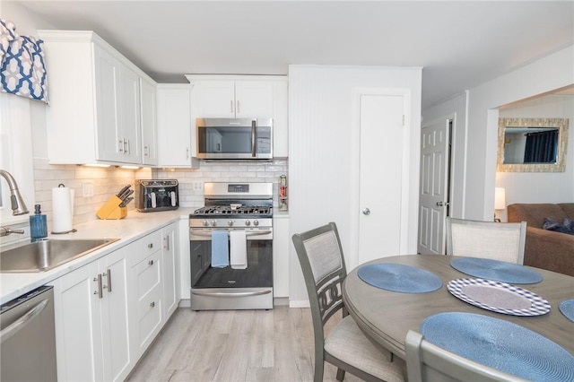 kitchen with white cabinets, light wood-style flooring, stainless steel appliances, light countertops, and a sink