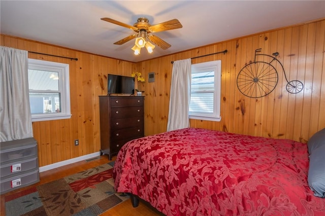 bedroom featuring visible vents, ceiling fan, wooden walls, wood finished floors, and baseboards