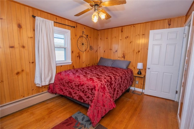 bedroom featuring a baseboard heating unit, crown molding, wood walls, and wood finished floors