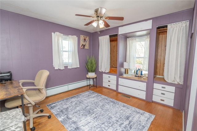 office area with light wood-style flooring, visible vents, a baseboard heating unit, and a wealth of natural light