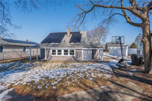 snow covered rear of property featuring fence and a chimney