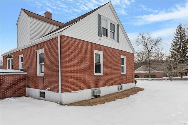 view of snow covered exterior with an AC wall unit, brick siding, and a chimney