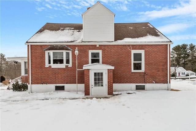 snow covered property featuring a chimney and brick siding