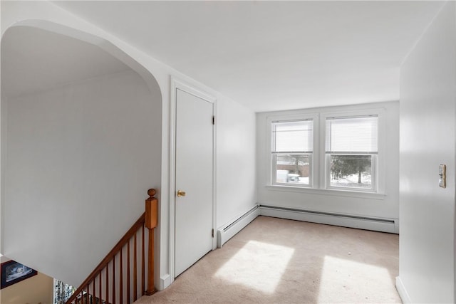 empty room with a baseboard radiator, light colored carpet, and arched walkways