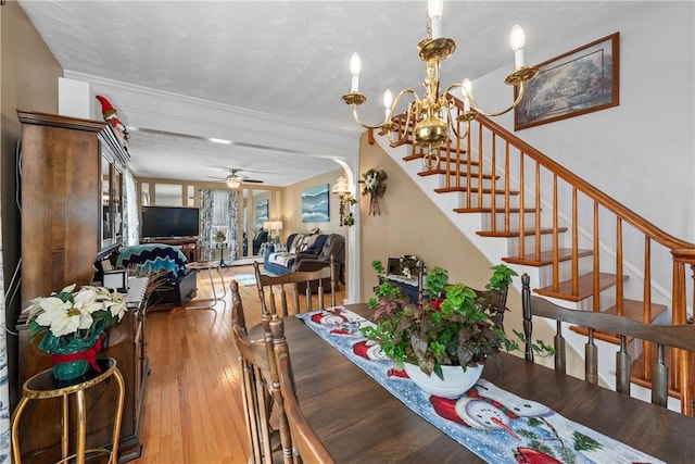 dining area featuring ceiling fan with notable chandelier, stairway, and wood finished floors