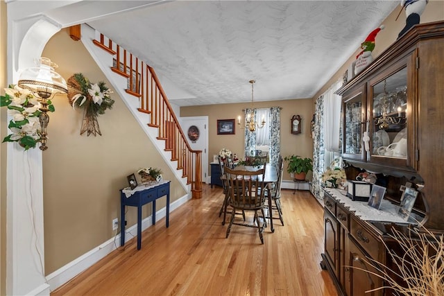 dining space with light wood-style flooring, a textured ceiling, a chandelier, baseboards, and stairs