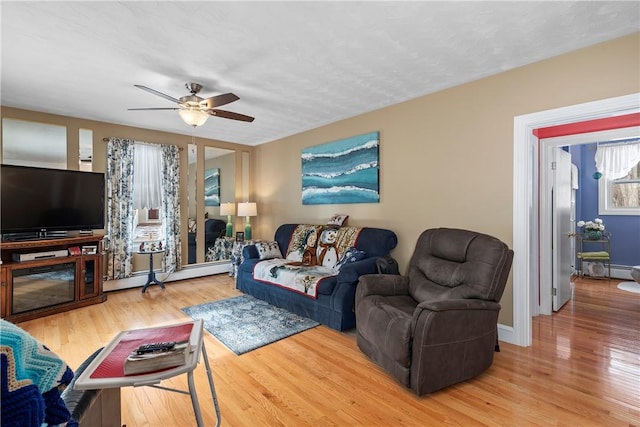 living area with a baseboard heating unit, ceiling fan, baseboards, and wood finished floors