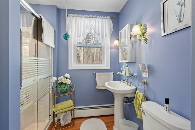 full bathroom featuring a shower, toilet, wood finished floors, a baseboard heating unit, and a sink