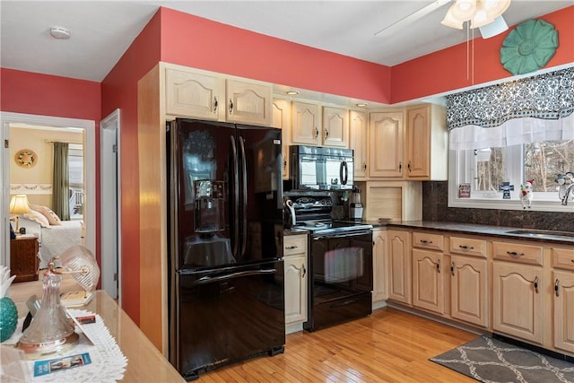 kitchen featuring light brown cabinets, a sink, light wood-style floors, black appliances, and dark countertops