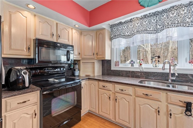 kitchen featuring light brown cabinets, a sink, light wood finished floors, and black appliances