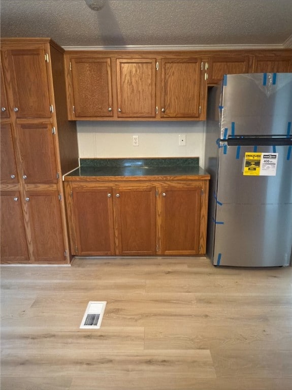 kitchen with brown cabinets, freestanding refrigerator, visible vents, and dark countertops