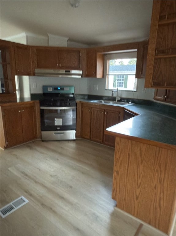 kitchen with under cabinet range hood, stainless steel gas range, visible vents, and brown cabinets