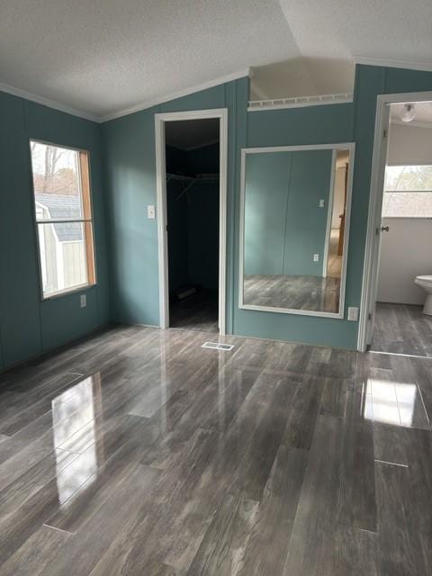 unfurnished bedroom featuring a textured ceiling, dark wood-type flooring, vaulted ceiling, ornamental molding, and a closet