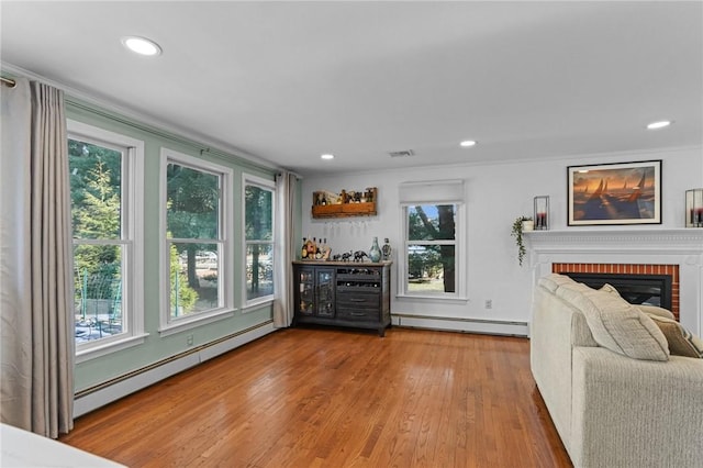 living room featuring a baseboard heating unit, visible vents, a fireplace, and wood finished floors