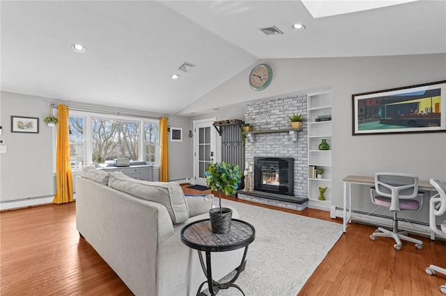 living area featuring visible vents, built in features, lofted ceiling with skylight, wood finished floors, and a brick fireplace