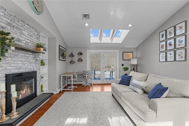 living room with vaulted ceiling with skylight, wood finished floors, visible vents, built in features, and a brick fireplace