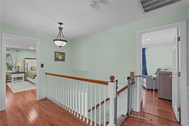 hall featuring baseboards, visible vents, an upstairs landing, and wood finished floors