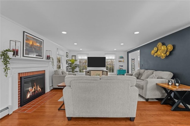 living area with crown molding, a fireplace, a baseboard heating unit, and wood finished floors