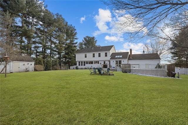 rear view of house with an outdoor structure, fence, a lawn, a storage unit, and a chimney