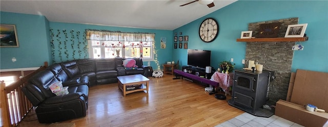 living room featuring a wood stove, ceiling fan, vaulted ceiling, and wood finished floors