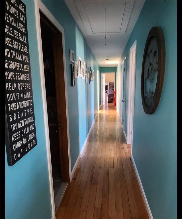 corridor featuring attic access, baseboards, and wood finished floors