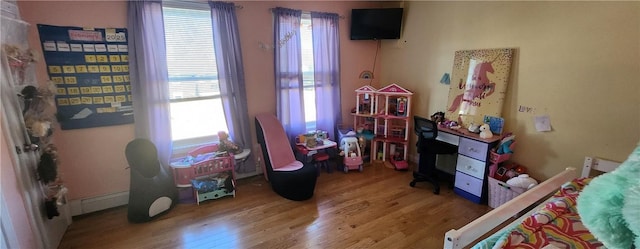 bedroom featuring multiple windows, baseboard heating, and wood finished floors