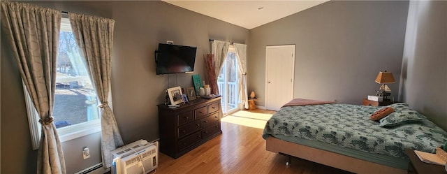 bedroom featuring a wall unit AC, vaulted ceiling, and light wood-style flooring